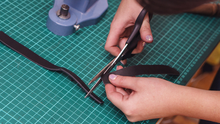 Tanner cuts off edges of leather product. Process of working in workshop close-up.