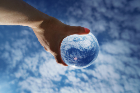 Contact juggling. Hand and acrylic ball on the background of the sky. Cumulus clouds reflected in the glass sphere. Close-upの写真素材