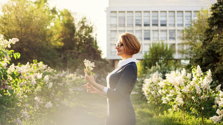 Attractive girl with glasses is holding lilac flowers in her hands. Evening walk after work. Woman in office style.の写真素材