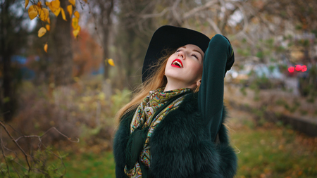 Red-haired girl in autumn park. She is wearing shorts and gloves and wide-brimmed hat. Woman is enjoying good weather.の写真素材