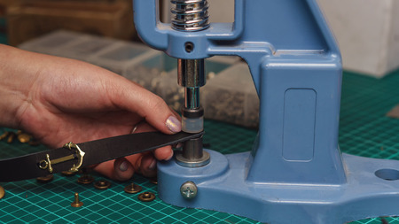 Tanner puts rivets on leather bracelet. Close-up photo. Process of working in workshop.の写真素材