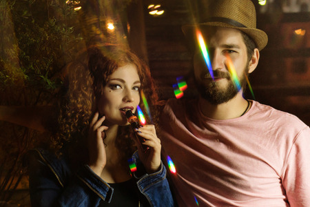 Loving couple on date. Guy and girlfriend smoke electronic cigarettes. They are together. Red-haired...