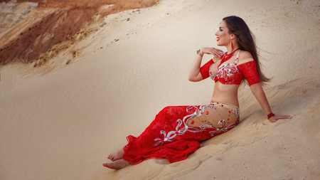 Oriental Beauty dancing sensual belly dance outdoors. Arab dance of seduction. Girl sat down on the sand dune.の写真素材