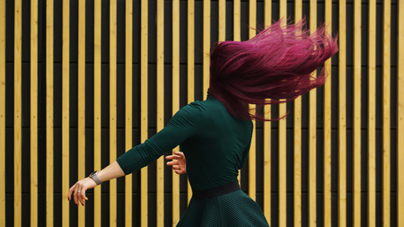 Cute young girl dancing on simple geometric background. Girl has eggplant hair flying in motion. Man unrecognizableの写真素材
