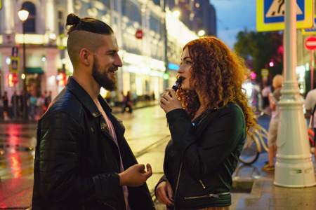 Couple in love on date. Boyfriend talking to girlfriend. She smokes an electronic cigarette. They...