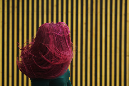 Cute young girl dancing on background of simple geometric pattern. Girl has eggplant hair flying in motion. She is in dark green dress. Man unrecognizableの写真素材