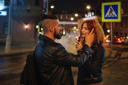 Couple in love on date. Boyfriend strokes girlfriend hair. She smokes an electronic cigarette. They...
