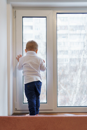 Little boy stands on windowsill and looks out window. Child is unrecognizable. Lonely childhood. Waiting for parents.の写真素材