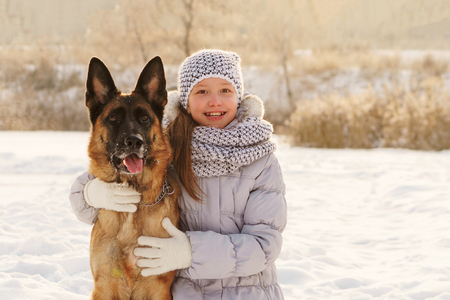Cute girl and German shepherd for walk. Sunny winter day. Girl hugging big pet and smilingの写真素材
