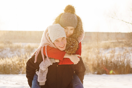 Adolescents in love on a date in winter. Guy carries his girlfriend piggyback. Joy of being together. First love. Concept for Valentine's Day.の写真素材