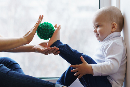 Mother makes foot massage to her son. She is holding massage ball. Little boy is smiling, he is tickled. Family care. Prevention of flatfootの写真素材