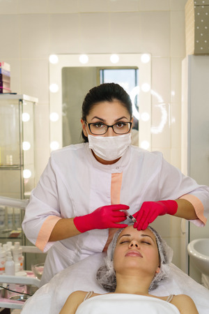 Girl in spa salon. Cosmetic procedure for rejuvenation. Face lift. Beautician holds syringe for injection.の写真素材