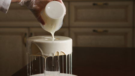 Confectioner fills cakes with white liquid mirror glaze.の写真素材