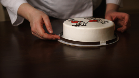 Confectioner attaches chocolate box to mousse cake. Baking with illustration of gift for Valentine's Day. Homemade pastry shop.の写真素材