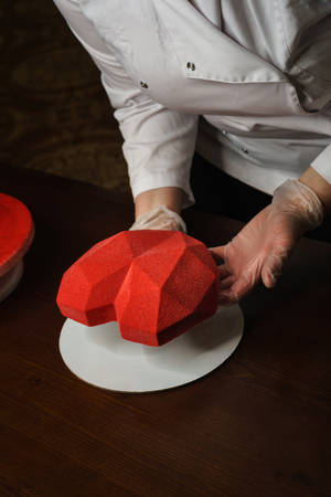 Confectioner places mousse cake in shape of heart on substrate. Origami form. Velor cover. Homemade pastry shop. Gift for Valentine's Day.の写真素材