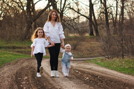 Happy family walking along path forest. Mother, oldest daughter and toddler, holding hands and gathering together. The concept of family ties. Spring moodの写真素材
