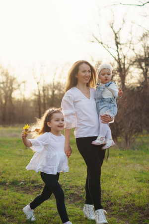 Happy young family on a walk in the spring meadow. Mom holds toddler in her arms. Girls in casual wear. Family look white clothes. Ð¡aught at the moment scamperの写真素材