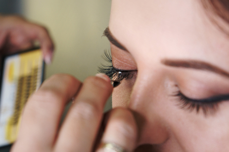 Makeup artist working in makeup studio attaches additional eyelashes to eyes. Close-up of a woman's...