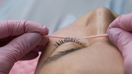 Eyelash extension procedure. Female eyes with long eyelashes. Cosmetic procedure in spa salon. Beautician corrects the shape of false eyelashesの写真素材