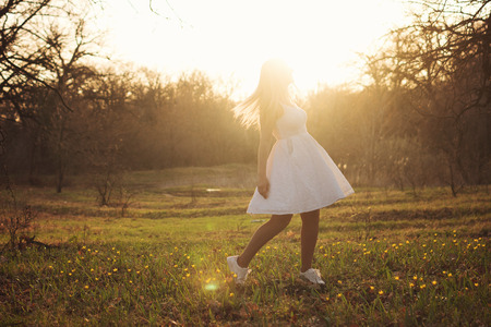 Girl dancing in white dress in spring meadow. Beauty in simplicity. Concept of freedom and unity with natureの写真素材