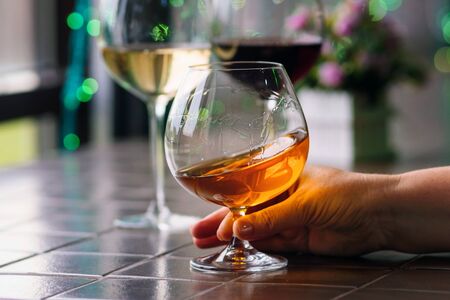 Female hand holding a glass of cognac. Relaxation concept. Cognac in glass on background of bright lights. Traditional French drinkの写真素材