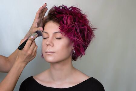 Makeup artist applies foundation concealer on your face model special brush. Work of professional beauty artist. Grey background. Beauty industry. Space for textの写真素材