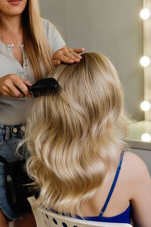 Beautiful model girl blonde with long curled hair. Creating hairstyle Hollywood wave. Hairdressing services. Hair styling process.の写真素材