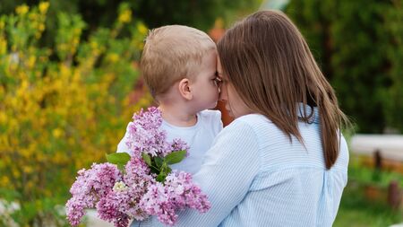 Young loving mother walking with her little son on spring background. Cute child and her mom on outdoor. Enjoy the good weather and spring flowers. Happiness to be a parent. Time together.の写真素材