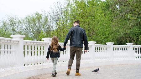 Fashionable stylish family for a walk. Dad and daughter walking on viewing platform holding hands. Excursion. Travel and tourism concept. Time together. Family look. Urban casual outfit. Back viewの写真素材
