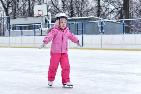 Beautiful girl having fun in winter park, balancing while skating at ice rink. Enjoying nature, winter time. Baby takes her first steps in figure skatingの写真素材