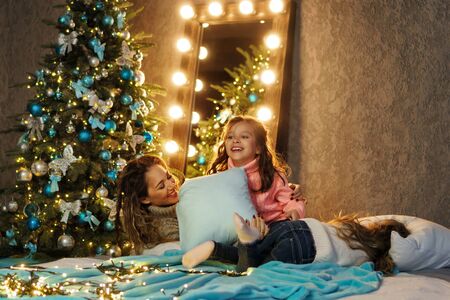 Lovely mum having fun while fighting pillows with her daughters in comfortable home interior,...