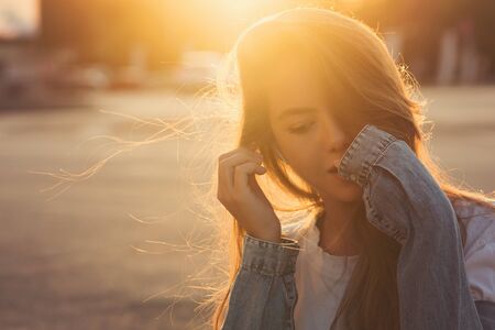 Back light portrait of a happy single teen girl breathing fresh air in a city street during a sunny day at sunset in a park with a warm yellow light and urban background. Summertime. Lifestyle.の写真素材