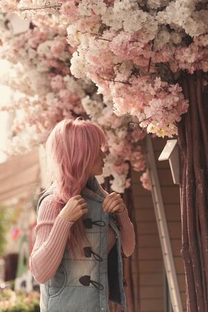 Lovely romantic young woman with long pink hair posing on a background of flowering tree. Inspiration of spring. Perfume concept.の写真素材