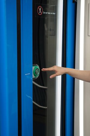 Woman hand index finger presses button to open doors in subway car. Public transport regulations,...