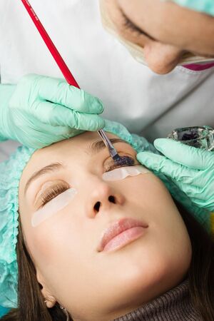Beauty treatment. Cosmetologist puts black paint on the lashes. Laminating eyelashes. Closeup eyes.