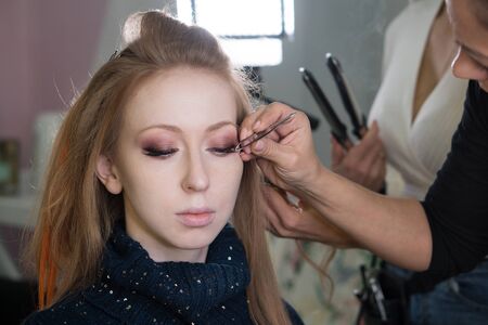 Beautiful girl applying false eyelashes with tweezers. Beauty woman with extreme long false...