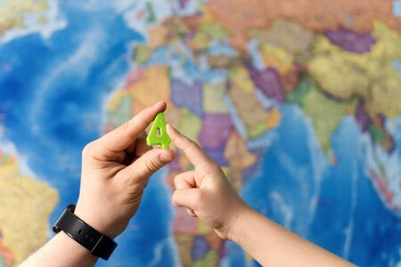 Adult and child hands holding numbers plastic toy on the world political map background. Travel planning explore destination concept. Family holidays and time together. Quarantine over, borders openの写真素材
