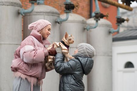 Happy family on walk with their funny terrier. Little dog with stylish hipster mom and son spend time outdoors playing and having fun. Lifestyle portrait. Love between pet and owner. Family timeの写真素材