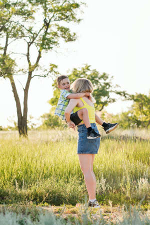 Young cheerful family in the meadow. Mom and son schoolboy spend time together and have fun in nature. Leisure. Summer holidays. Summertime. Happy childhood and motherhoodの写真素材