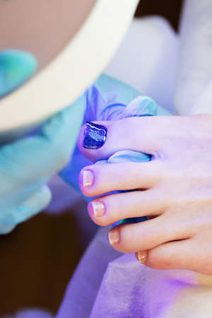 Close up view of female leg with fresh beautiful gel polish pedicure. Woman puts foot into led uv lamp for curing cover of nailpolish.の写真素材