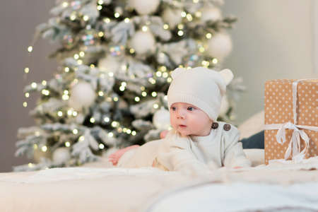 Tiny little child celebrates its first Christmas among gift boxes and Christmas lights. Christmas...