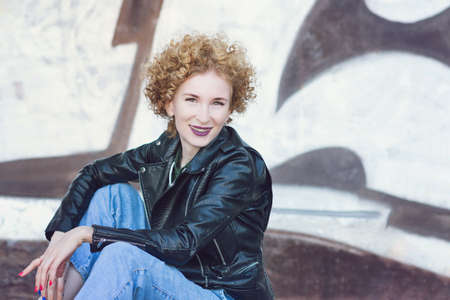 Smiling young woman with curly hairstyle. Girl in casual clothes in the street. Fashionista girl...