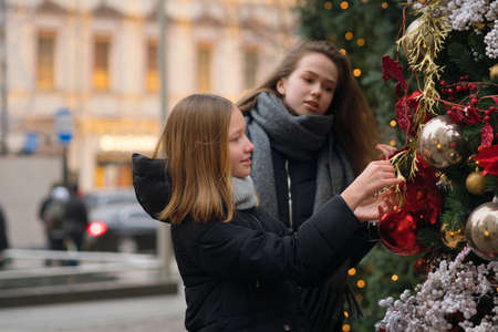 Two female best friends on Christmas Market. Adorable sisters having fun together on traditional Christmas fair. Winter time with family. Girls enjoying the scenery and atmosphere on Xmas market.の写真素材