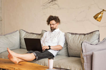 Man Sitting On Sofa At Home Using Laptop Computer. Working From Home During Pandemic Lockdown. Freelance. Homesourcing. Home Officeの写真素材