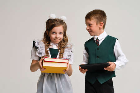 Portrait two elementary school students in uniform with books and tablet pc. New technologies for...