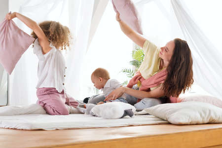 Family Wearing Pyjamas Wake Up Early In Morning. Pillow Fight In Comfortable Bedroom Home.