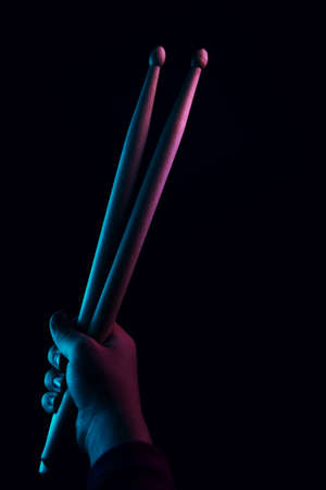 Child Hand Hold Wooden DrumSticks On Black Background Backlit Colorful Vivid Neon. Rock Music Concept. Unrecognizable. Advertising Drum Lessons For Children. Soft Focusの写真素材