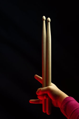 Child Hand Hold Wooden Drum Sticks. Showing Devil Horns Sign, Symbol Of Heavy Metal On Black Backlit Red Background. Rock Music Concept. Unrecognizable. Soft Focusの写真素材