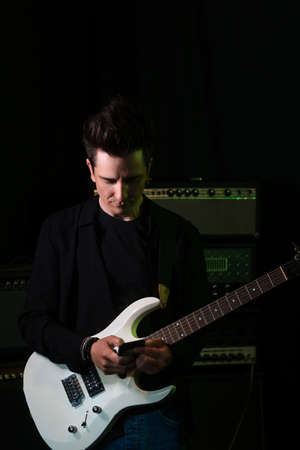 Handsome male musician with electric guitar in recording studio. Rock musician holding smartphone on...