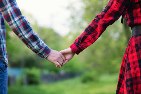 Unrecognizable romantic couple holding hands in nature. Close-up shot of man and woman with hand to hand walking on a grassy field.の写真素材